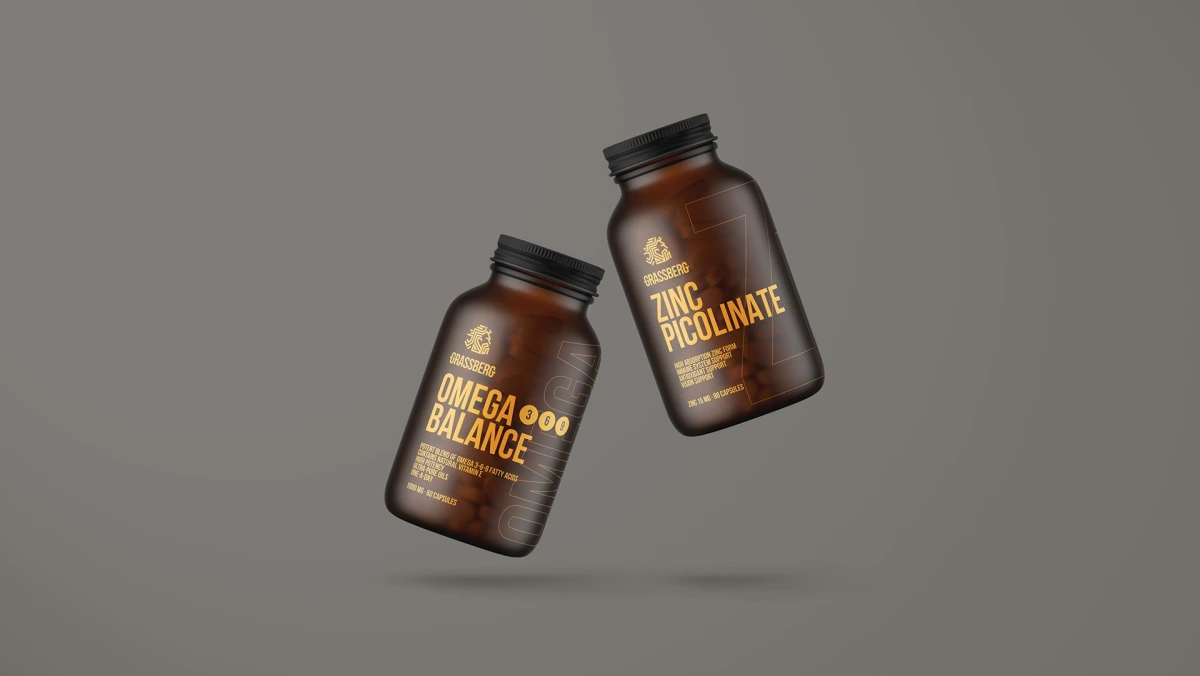 Grassberg Omega Balance and Zinc Picolinate bottles tilted against grey background