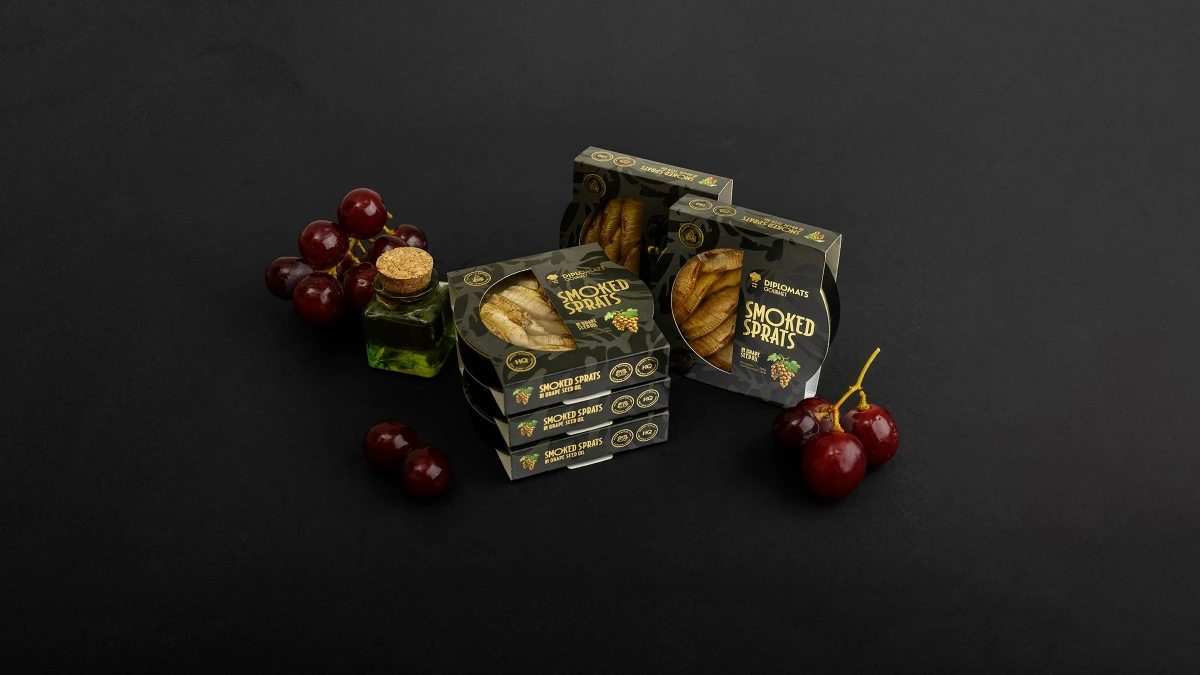 Diplomats Smoked Sprats boxes with olive oil bottle, grapes and cherries on black background